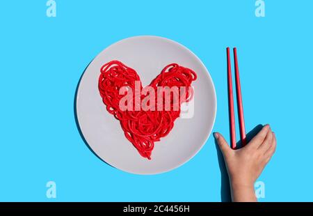 Main de bébé fille atteignant pour des baguettes de manger rouge-couleur coeur-forme spaghetti Banque D'Images