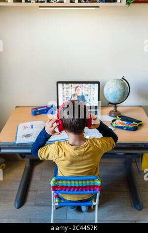 Vue arrière de l'élève écoutant son professeur à travers des écouteurs pendant le homeschooling Banque D'Images