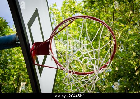 vue rapprochée et descendante du terrain de basket-ball avec cerceau rouge et filet dans les feuilles d'arbres du parc comme arrière-plan Banque D'Images