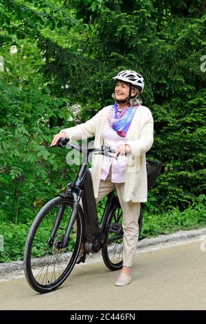 Femme âgée heureuse debout avec vélo électrique sur la piste de marche dans le parc Banque D'Images