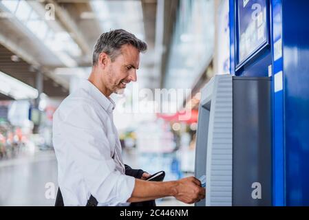 Homme d'affaires retirant de l'argent par distributeur automatique de billets à la gare Banque D'Images