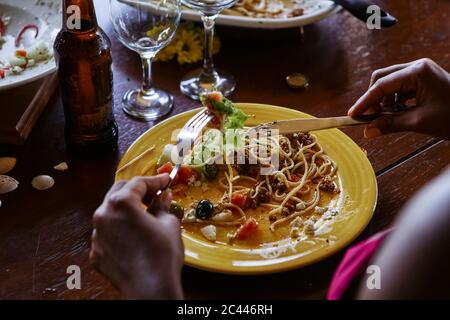 Section moyenne de la jeune femme mangeant des pâtes à la table à manger Banque D'Images