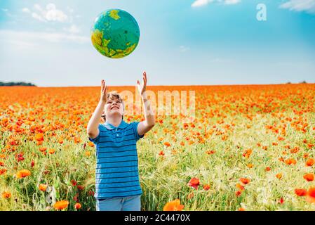 Happy boy attraper globe tout en se tenant dans le champ de pavot contre ciel sur sunny day Banque D'Images