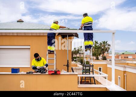 Techniciens mâles installant des panneaux solaires sur le toit de la maison contre le ciel nuageux Banque D'Images