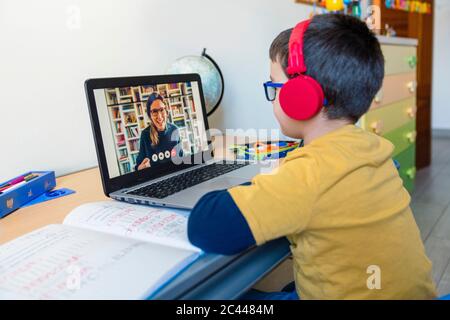 Garçon écoutant son professeur à travers un casque pendant un appel vidéo à la maison Banque D'Images