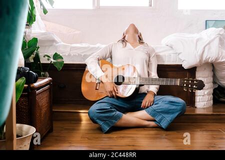 Femme avec guitare assise sur le sol devant le lit, penchée vers l'arrière Banque D'Images