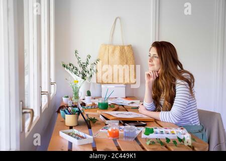 Jeune femme attentionnés qui regarde loin tout en peignant sur une table à la maison Banque D'Images