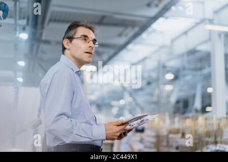 Homme d'affaires mature avec des documents et une tablette dans une usine Banque D'Images