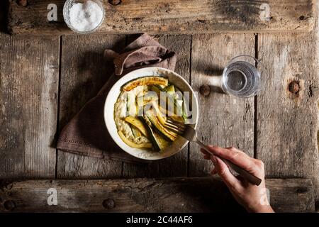 La main coupée de mature woman eating meal on wooden table Banque D'Images