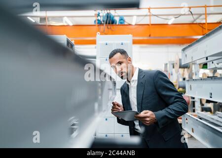 Homme d'affaires avec tablette dans des tiges métalliques dans le hall d'usine Banque D'Images