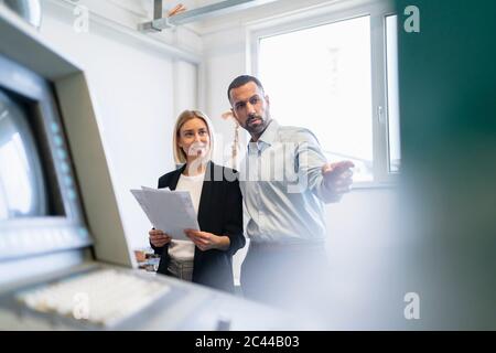 Homme d'affaires et femme avec du papier à une machine dans le hall d'usine Banque D'Images