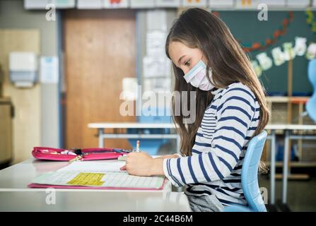 Fille portant un masque en classe écrivant dans le cahier d'exercices Banque D'Images