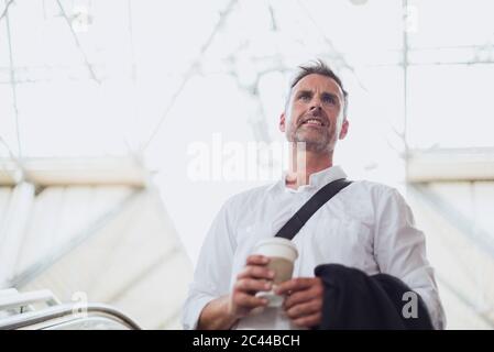 Homme d'affaires attentionné qui tient le café en regardant loin tout en se tenant sur l'escalier roulant Banque D'Images