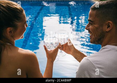 Un jeune couple joyeux se regardant les uns les autres tout en dorant des verres contre la piscine Banque D'Images