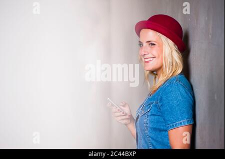 Portrait d'une jeune femme heureuse avec un smartphone appuyé contre le mur Banque D'Images