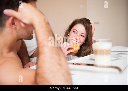 Bonne femme mangeant un croissant en regardant l'homme dans la chambre Banque D'Images