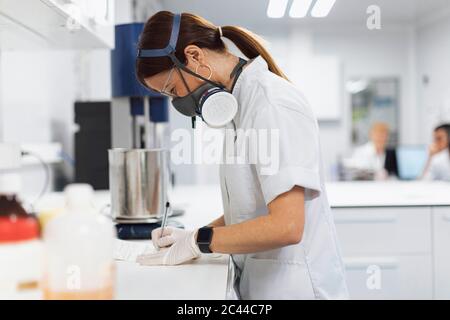 Une femme mature, technicienne pharmaceutique, écrit des données sur le bureau en laboratoire Banque D'Images