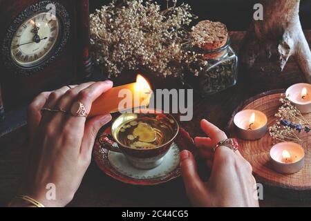 Sorcière wiccan femelle portant des bijoux vintage tenant une bougie jaune et versant de la cire dans un rouge blanc or couleur vintage teacup comme méthode de divination Banque D'Images