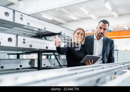 Homme d'affaires et femme avec tablette dans des tiges métalliques dans le hall d'usine Banque D'Images