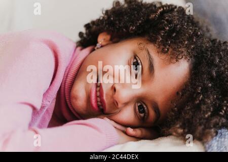 Portrait d'une petite fille souriante portant un pull à col roulé rose allongé sur un canapé Banque D'Images