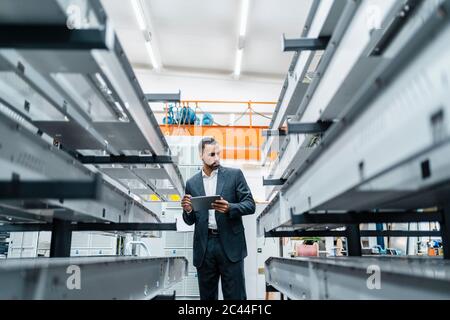 Homme d'affaires avec tablette dans des tiges métalliques dans le hall d'usine Banque D'Images