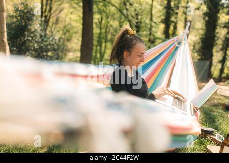 Jeune femme utilisant un ordinateur portable tout en étant assise sur un hamac dans la cour Banque D'Images