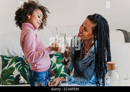 Une mère heureuse et sa petite fille avec un verre de lait à la maison Banque D'Images