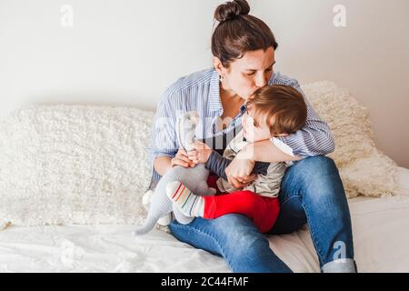 Mère assise sur le lit embrassant bébé garçon Banque D'Images