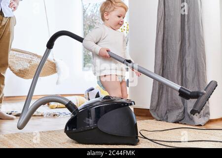 Un adorable tout-petit tenant un aspirateur tout en se tenant debout sur la moquette par son père à la maison Banque D'Images