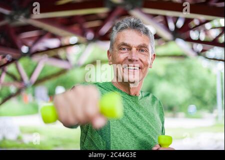 Portrait d'un homme âgé souriant qui s'exerce avec des haltères tout en se tenant au belvédère dans le parc Banque D'Images