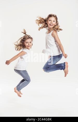 Portrait de deux sœurs pieds nus sautant dans l'air devant un fond blanc Banque D'Images