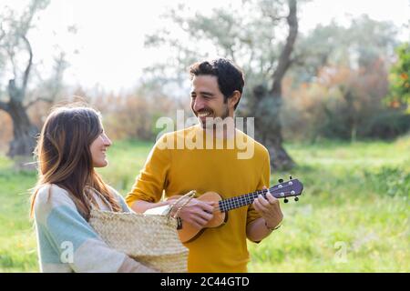 Femme portant un panier en osier pendant que l'homme heureux joue de la guitare à la campagne Banque D'Images