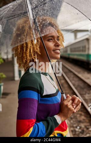 Vue latérale de la jeune femme avec la coiffure afro appréciant la mousson en se tenant à la gare Banque D'Images