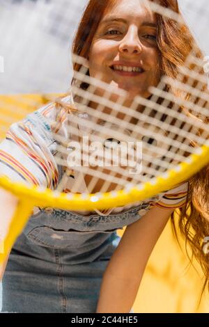 Bonne jeune femme regardant à travers la raquette de badminton pendant la journée ensoleillée Banque D'Images