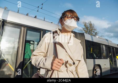 Femme portant un masque de visage en train de descendre du bus en ville Banque D'Images