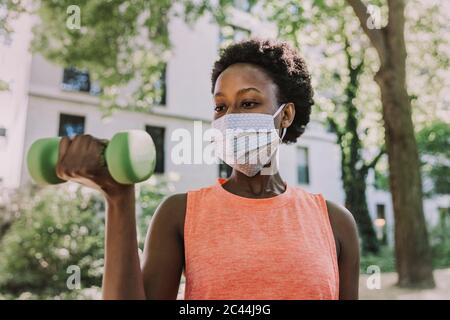 Portrait de femme portant un masque de protection s'exerçant avec haltère à l'extérieur Banque D'Images