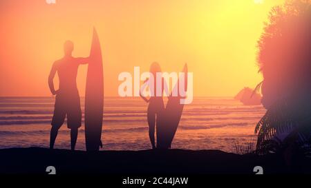 Silhouettes de surfeurs illuminées par le soleil couchant. Banque D'Images