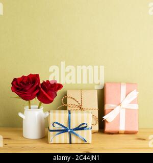 Boîtes-cadeaux avec fleurs roses rouges dans un vase sur une table en bois avec fond kaki. Concept anniversaire, arrangement floral, espace de copie Banque D'Images