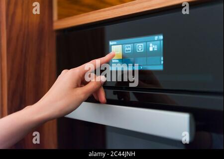 Femme touchant l'affichage numérique du four dans la cuisine Banque D'Images