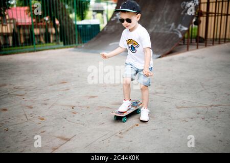 Garçon avec un skate dans un parc de skate. Un garçon avec des lunettes apprend à skate. Banque D'Images