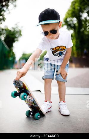 Garçon avec un skate dans un parc de skate. Un garçon avec des lunettes apprend à skate. Banque D'Images
