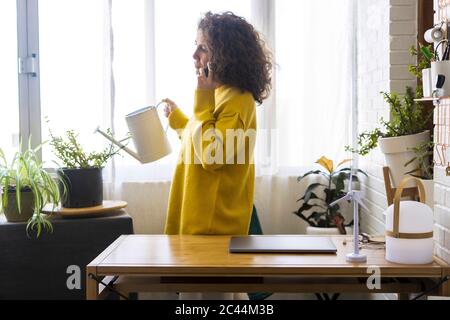 Femme au téléphone dans les usines d'arrosage de bureau à domicile Banque D'Images