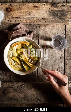 La main coupée de woman eating hoummos avec courgettes frites on wooden table Banque D'Images