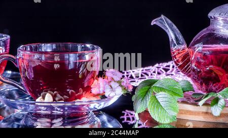 Une tasse de thé rouge et une théière en fleurs d'hibiscus blanc et feuilles vertes de thé médicinal sur un stand en bois.cérémonie du thé Zen. Photo de l'Indi rouge Banque D'Images