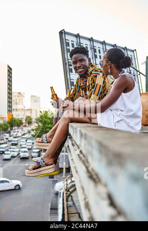 Couple assis sur la terrasse sur le toit dans la ville de boire de la bière, Maputo, Mozambique Banque D'Images