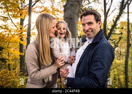 Homme souriant portant sa fille en étant debout par une femme enceinte en forêt Banque D'Images