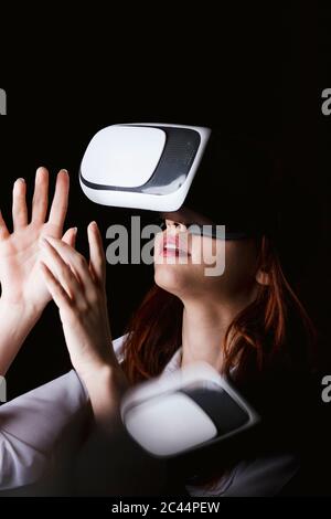 Jeune femme qui fait des gestes avec des lunettes VR sur fond noir Banque D'Images