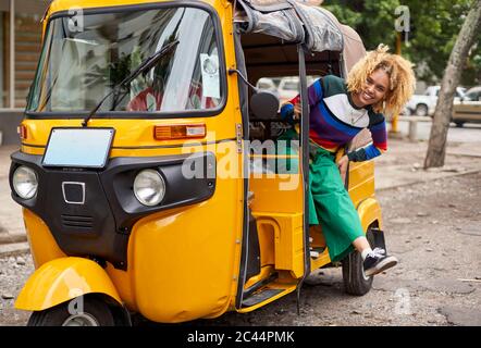 Portrait complet de la jeune femme souriante s'appuyant sur le tuk-tuk en ville Banque D'Images