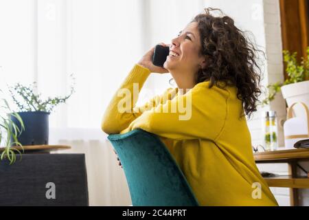 Bonne femme brunette parlant au téléphone dans le bureau à la maison Banque D'Images