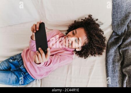 Portrait de la fillette heureuse couché sur le canapé à l'aide d'un smartphone Banque D'Images